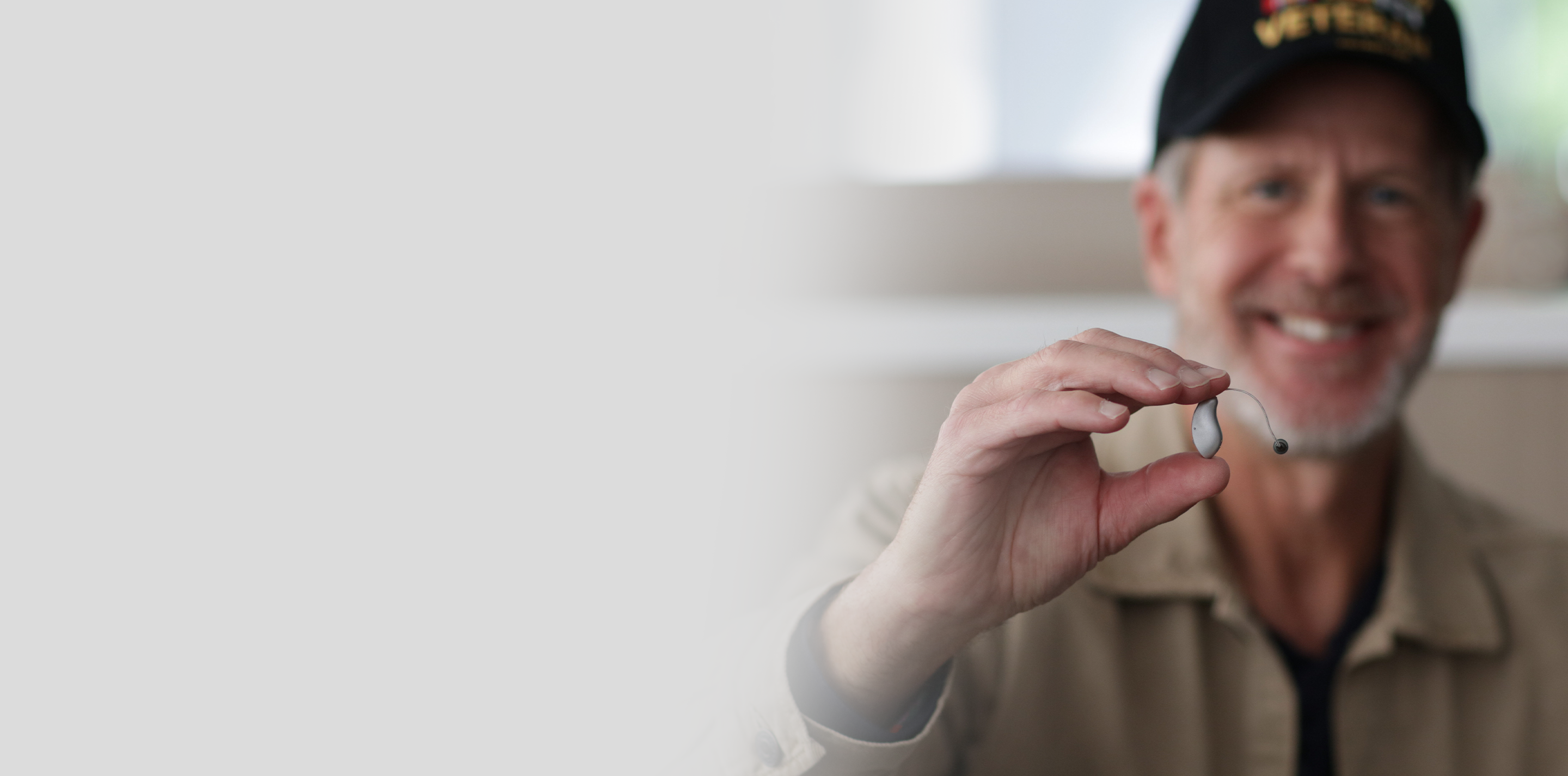 Veteran holding hearing aid.