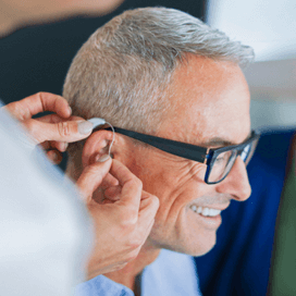 Starkey History 2016 - Man wearing glasses being fit with a hearing aid