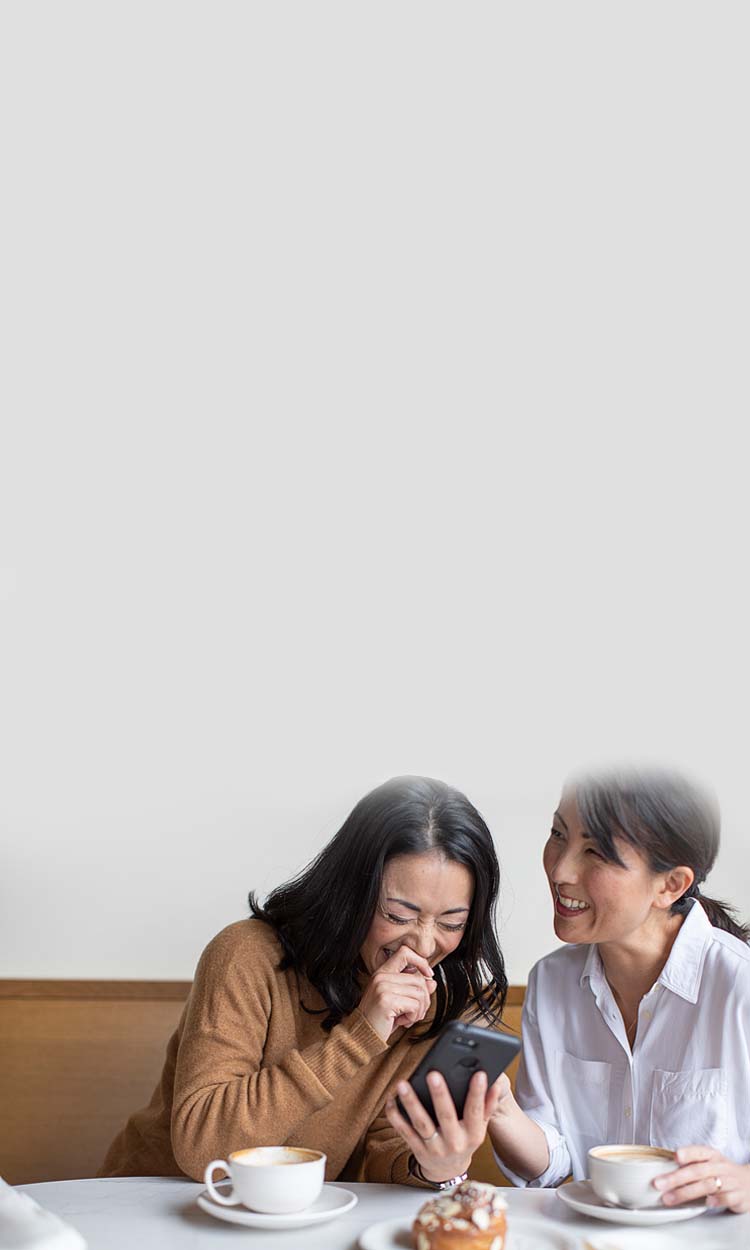 Two women laughing looking at a phone while drinking coffee