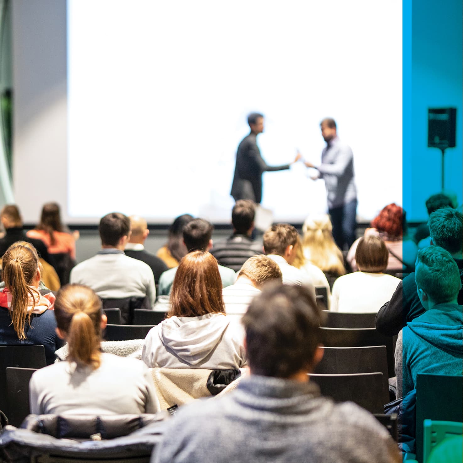 two people exchanging an item on stage in from of a crowd of students