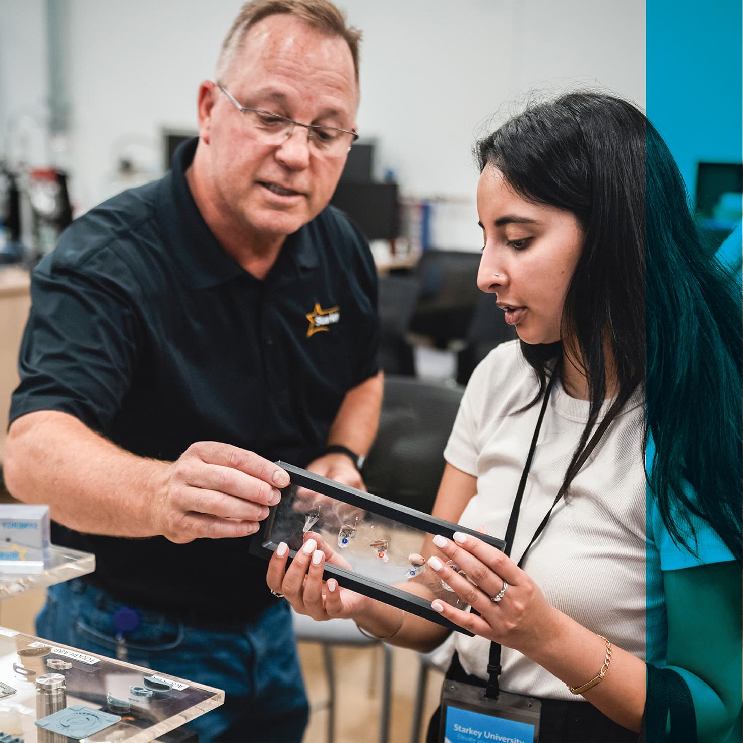 man showing a student a glass plate hearing aid diorama